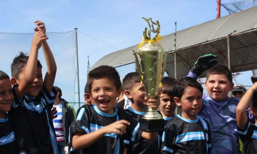 Niños celebrando triunfo en torneo de fútbol con copa en las maos